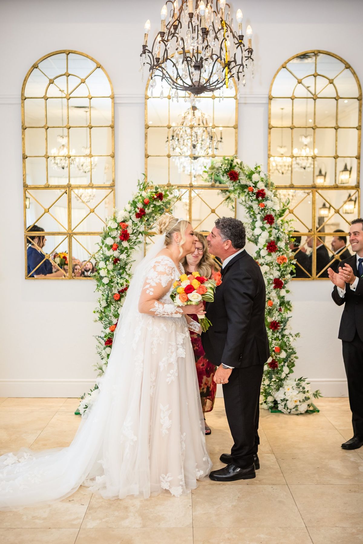 The couple's kiss at a red and white floral arch