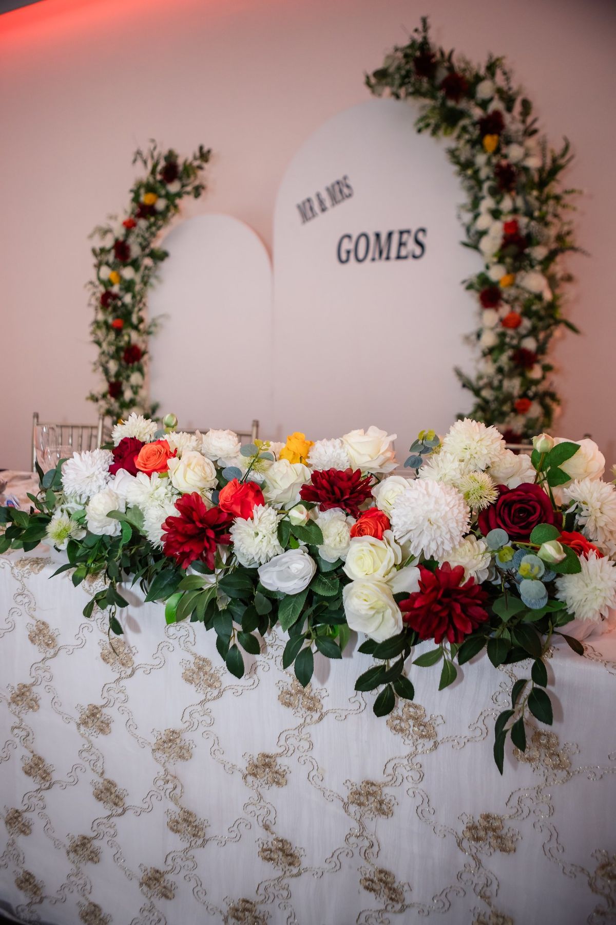 Head table dressed with red, white and orange florals before a floral arch