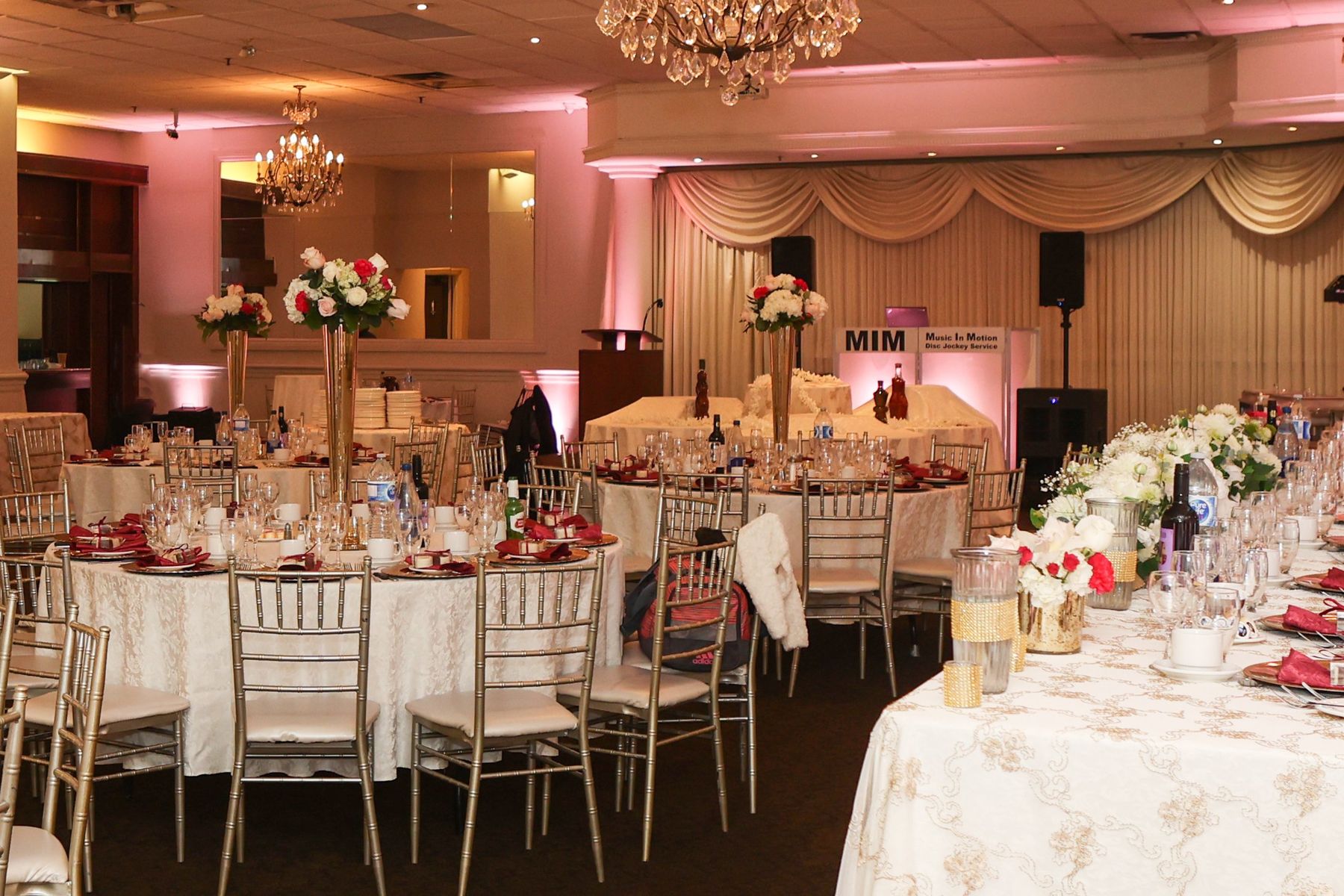 A ballroom set with tall gold centerpieces, with the Music In Motion DJ booth at the back