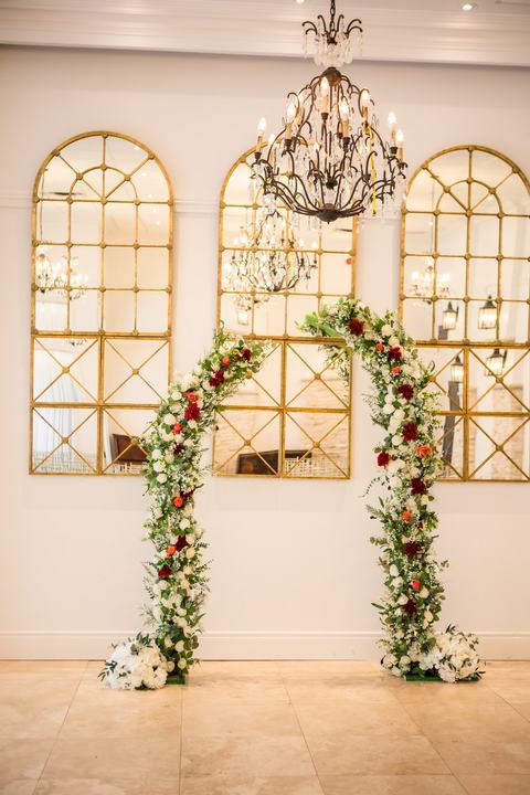 Red and white floral arch in front of gold arched mirrors