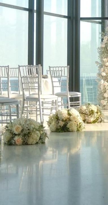 Sunroom ceremony aisle floral clusters, white chairs