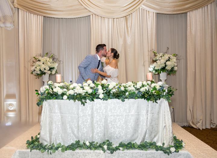 Couple kiss behind sweetheart table, champagne drapery