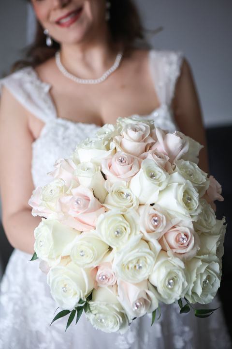 A bride holding a blush and white rose bouquet with pearls
